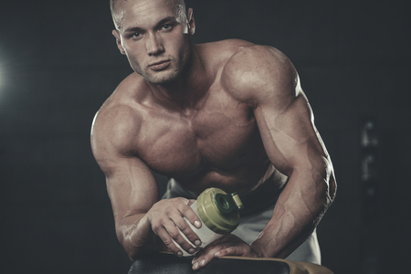 Handsome young muscular Caucasian man of model appearance taking protein sports nutrition in the gym and poses fitness and bodybuilding conceptの写真素材