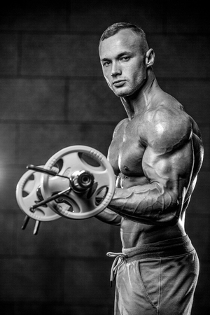 Handsome muscular Caucasian man of model appearance working out training arms in gym gaining weight pumping up muscles bicep and tricep with dumbbells and on machines fitness and bodybuilding conceptの写真素材