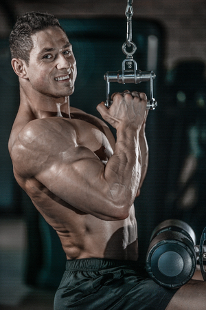 Handsome young muscular Caucasian man of model appearance working out training pumping up back lats muscles in the gym gaining weight on machines posing fitness and bodybuilding conceptの写真素材