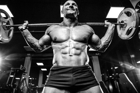 Handsome young muscular Caucasian man of model appearance working out in the gym training legs quadriceps and hamstrings on machines and with a barbell pumping up fitness and bodybuilding conceptの写真素材
