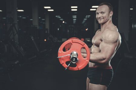Handsome muscular Caucasian man of model appearance working out training arms in gym gaining weight...