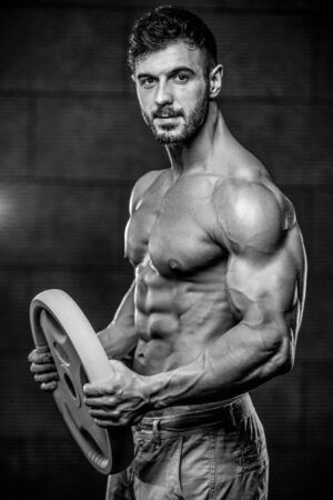 Handsome muscular Caucasian man of model appearance working out training arms in gym gaining weight pumping up muscles bicep and tricep with dumbbells and on machines fitness and bodybuilding conceptの写真素材