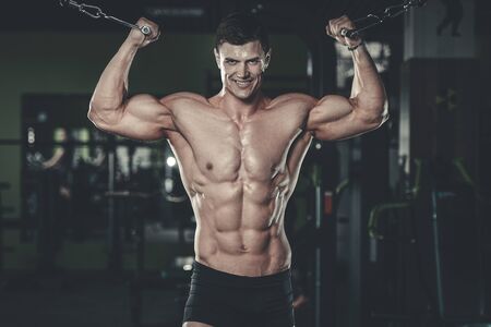 Attractive young muscular sexy Caucasian man of model appearance working out training in the gym gaining weight pumping up muscles and poses fitness and bodybuilding conceptの写真素材