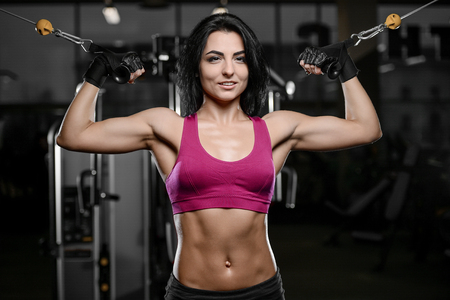 Beautiful brunette sexy athletic muscular young brunette Caucasian fitness girl working out training in the gym gaining weight pumping up abs muscles and poses bodybuilding health care conceptの写真素材