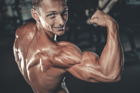 Handsome muscular Caucasian man of model appearance working out training arms in gym gaining weight pumping up muscles bicep and tricep with dumbbells and on machines fitness and bodybuilding conceptの写真素材