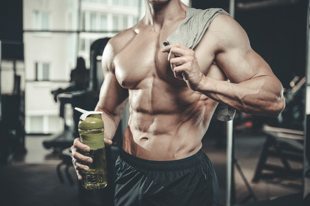 Handsome young muscular Caucasian man of model appearance taking protein sports nutrition in the gym and poses fitness and bodybuilding conceptの写真素材