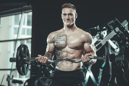 Handsome young muscular Caucasian man of model appearance working out training in the gym gaining weight pumping up muscles and poses fitness and bodybuilding conceptの写真素材