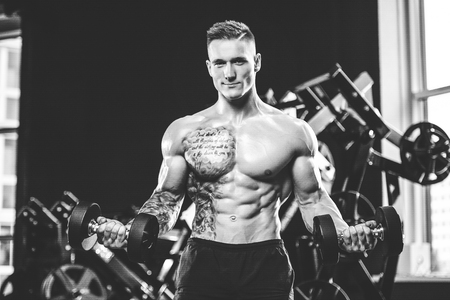 Handsome muscular Caucasian man of model appearance working out training arms in gym gaining weight pumping up musclesの写真素材