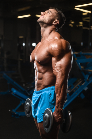 Handsome young fit muscular caucasian man of model appearance workout training in the gym gaining weight pumping up muscle, poses, drinks water  fitness and bodybuilding sport nutrition conceptの写真素材