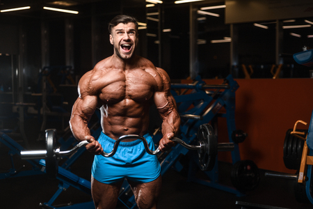 Handsome young fit muscular caucasian man of model appearance workout training in the gym gaining weight pumping up muscle, poses, drinks water  fitness and bodybuilding sport nutrition conceptの写真素材