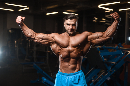 Handsome young fit muscular caucasian man of model appearance workout training in the gym gaining weight pumping up muscle, poses, drinks water  fitness and bodybuilding sport nutrition conceptの写真素材