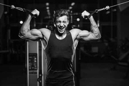 Handsome young fit muscular caucasian man of model appearance workout training in the gym gaining weight pumping up muscles and poses fitness and bodybuilding sport conceptの写真素材