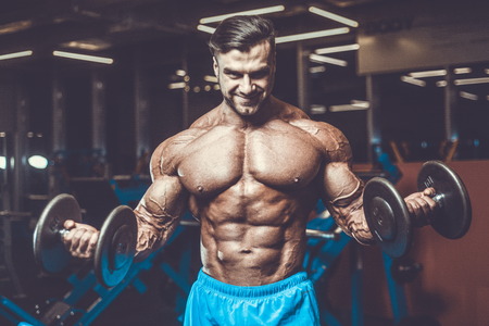 Handsome young fit muscular caucasian man of model appearance workout training in the gym gaining weight pumping up muscle, poses, drinks water  fitness and bodybuilding sport nutrition conceptの写真素材