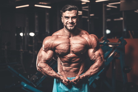Handsome young fit muscular caucasian man of model appearance workout training in the gym gaining weight pumping up muscle, poses, drinks water  fitness and bodybuilding sport nutrition conceptの写真素材