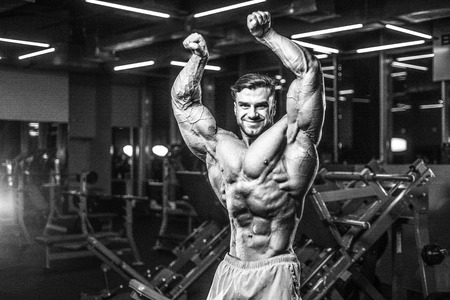 Handsome young fit muscular caucasian man of model appearance workout training in the gym gaining weight pumping up muscle, poses, drinks water  fitness and bodybuilding sport nutrition conceptの写真素材
