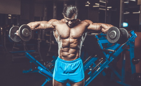 Handsome young fit muscular caucasian man of model appearance workout training in the gym gaining weight pumping up muscle, poses, drinks water  fitness and bodybuilding sport nutrition conceptの写真素材