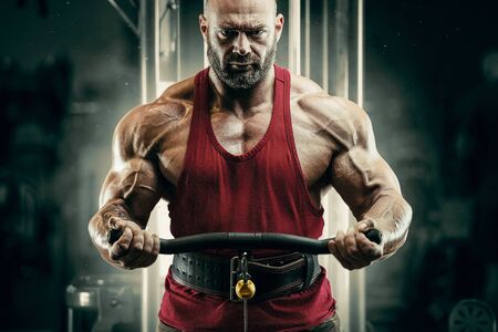 Bodybuilder handsome strong athletic rough man pumping up biceps muscles workout fitness and...