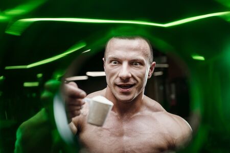Fitness man at workout in gym with protein powder jar. Bodybuilding and healthy lifestyle concept background. Muscular bodybuilder with sport nutrition supplements jar in gym naked torsoの写真素材