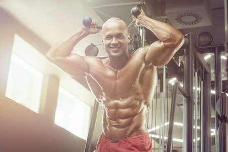 Bodybuilder handsome strong athletic rough man pumping up triceps muscles workout fitness and...