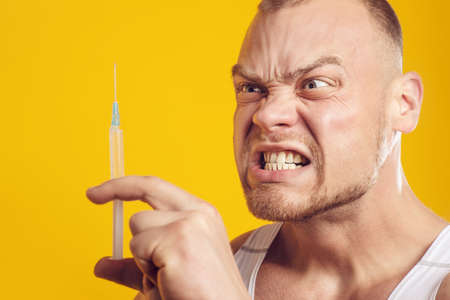 Studio portrait of muscular man with pill and syringe, injector, standing over isolated yellow background. Fitness, bodybuilding and work out conceptの写真素材
