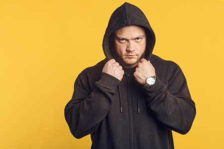Studio portrait of muscular man in a black hood and a mask, standing over isolated yellow background. Fitness, bodybuilding and work out conceptの写真素材