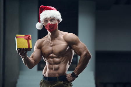 Fitness man in Santa Claus hat costume in gym with a gift box. Merry Christmas conceptの写真素材