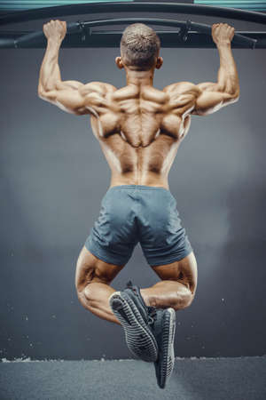 Fitness man pumping up muscle doing pull-ups exercises in gym naked torso. Handsome strong athletic men pumping up back muscles workout fitness and bodybuilding concept backgroundの写真素材