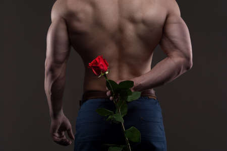 Athletic man holding a red rose behind his back. Love and romance relationships concept