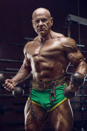 Old fashion athlete bodybuilder doing arm exercises in gym. Brutal bald caucasian sports man style of the 80s. Sport, fitness and workout 80s conceptの写真素材