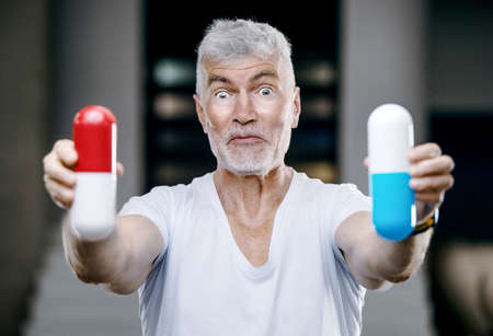 Emotional Handsome gray haired senior man with a big red and blue pill in his hand. Medicine and health care conceptの写真素材