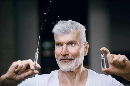Emotional Handsome gray haired senior man vaccinated with a syringe in hand. Immunization and health care conceptの写真素材