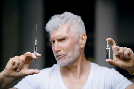 Emotional Handsome gray haired senior man vaccinated with a syringe in hand. Immunization and health care conceptの写真素材