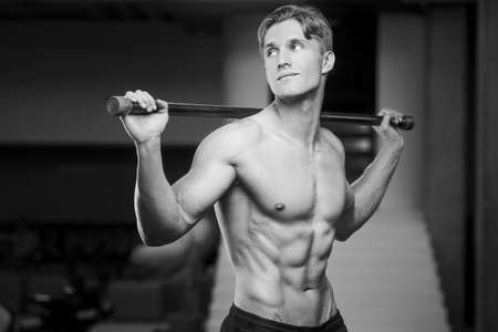 Young athletic man pumping up muscles in the gym at workout. Sport and health care concept backgroundの写真素材