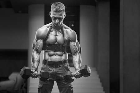 Young athletic man pumping up muscles in the gym at workout. Sport and health care concept backgroundの写真素材