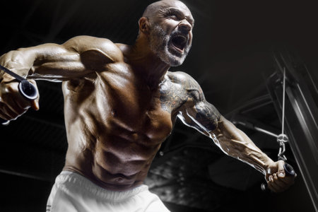 Brutal and muscular strong bodybuilder athletic man pumping up muscles at workout in the gym. Sport and health care concept backgroundの写真素材
