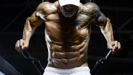 Brutal and muscular strong bodybuilder athletic man pumping up muscles at workout in the gym. Sport and health care concept backgroundの写真素材
