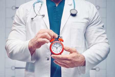 The doctor holds alarm clock in his hands. Health care conceptの写真素材