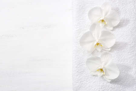 Three orchids and white terry towel  lying on shabby wooden board.  Viewed from above. Spa concept.の写真素材