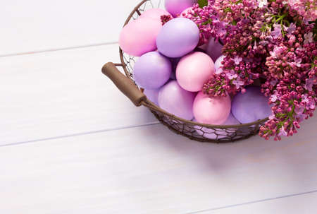 Easter eggs and  lilac  flowers on  pink wooden table. View from above.