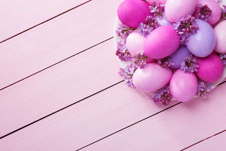 Easter eggs and  lilac  flowers on  pink wooden table. View from above.