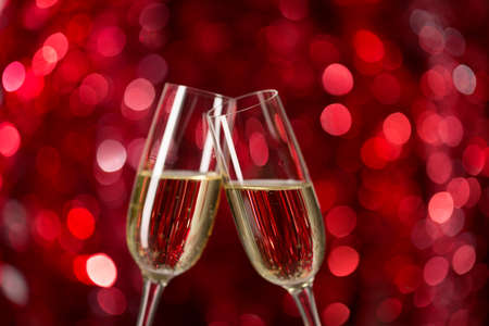 Two glasses of champagne against red background with sparkles. Very shallow depth of field. Selective focusの写真素材