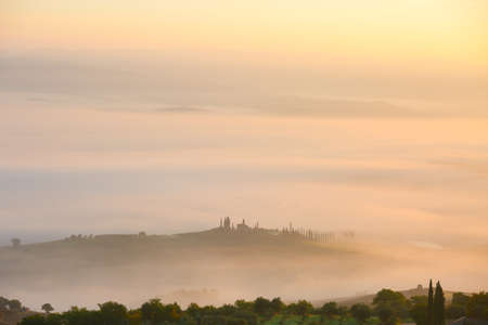 Picturesque view of foggy rolling fields of Tuscany in the light of the rising sun, Italy.の写真素材