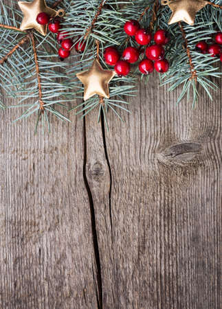 Fir branch with red berries and golden stars on an old wooden board with copy space for text. Christmas and New Year holidays background. Selective focus.の写真素材