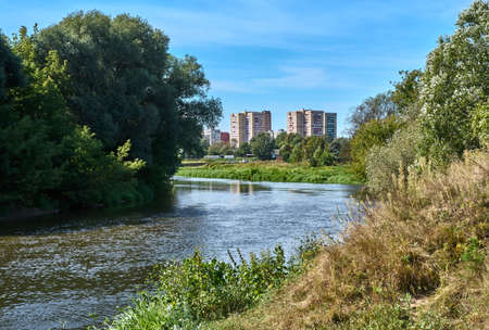 A river with trees on the shore and a city against the backdrop of a clear warm dayの写真素材