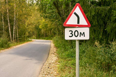 Road sign dangerous turn after 30 meters on a car road in the forestの写真素材