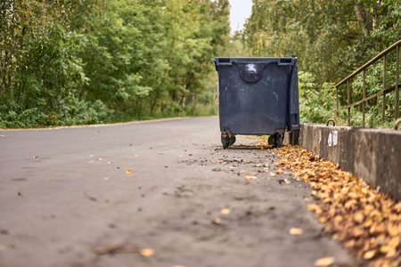 Black open trash can on wheels stands on a concrete road in an autumn dayの写真素材