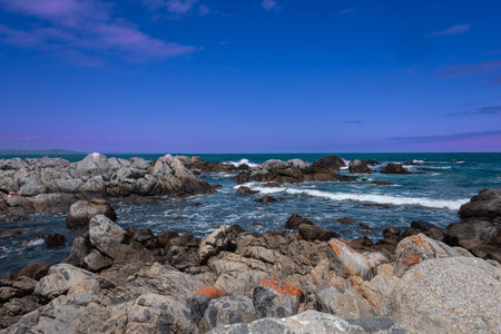 A glimpse of the Pacific Ocean in central Chile with rocks and pink clouds.