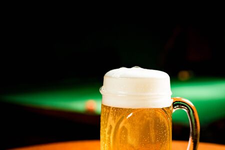 Mug with draft beer on a table with pool table behindの写真素材