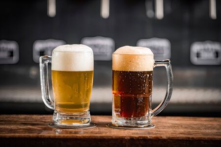 Two mugs full of chopp, one with chopp and one with dark chop on a rustic tableの写真素材