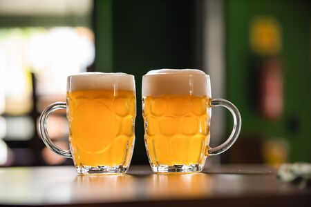 two mugs full of chopp, with chopp on a rustic table